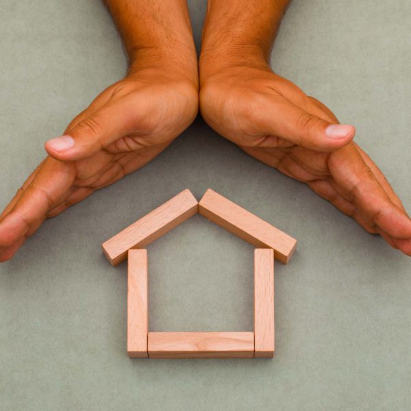 Mortgage concept on greenish grey background flat lay. hands enclosing wooden house.